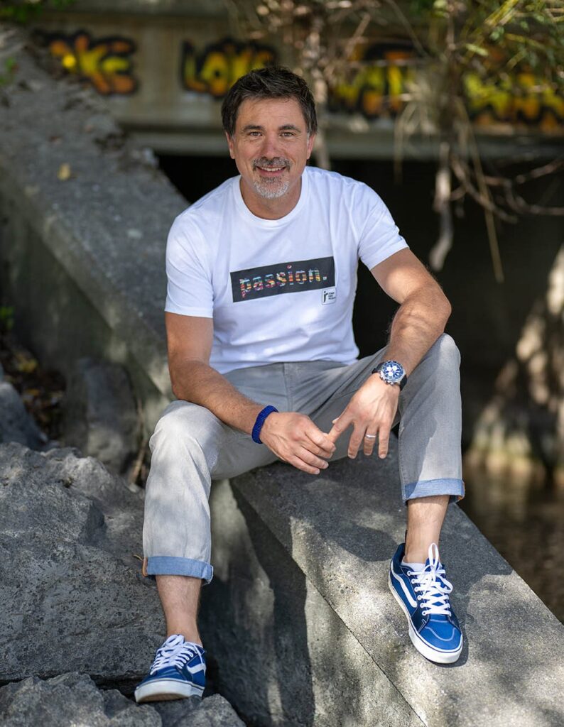 Strategischer Coach Patrick Murnig sitzend auf einer Mauer, blickt freundlich in die Kamera.